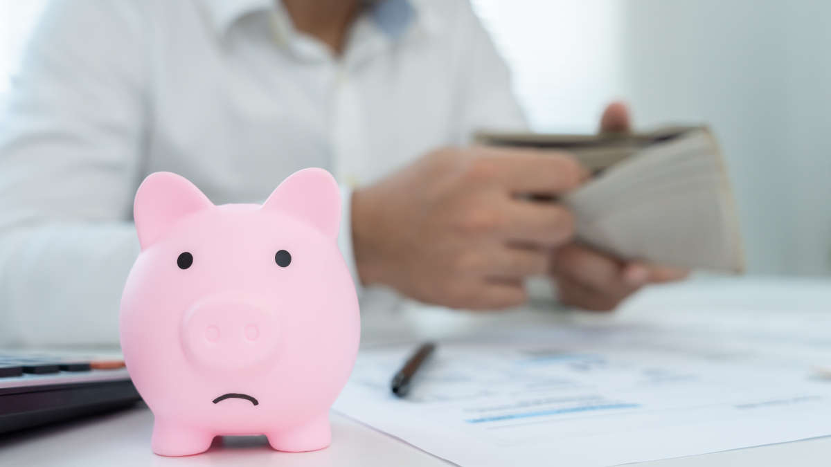 Person mit leerem Portmonee, vorne Sparschwein, traurig