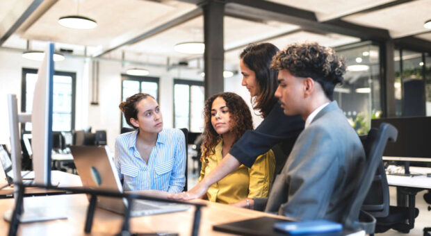 Drei junge Personen hören in einem Büro einer etwas älteren Person zu.