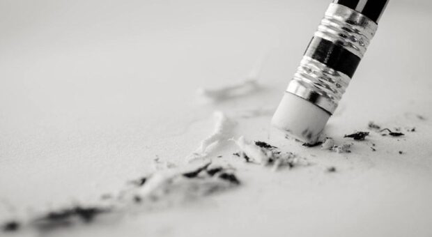 Radiergummi am Ende eines Bleistiftsts, der auf einem Blatt etwas wegradiert.