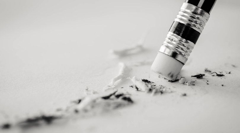 Radiergummi am Ende eines Bleistiftsts, der auf einem Blatt etwas wegradiert.