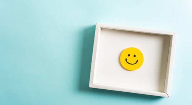 Gerahmtes Bild mit einem lachenenden Smiley, das an einer türkisfarbenen Wand hängt.