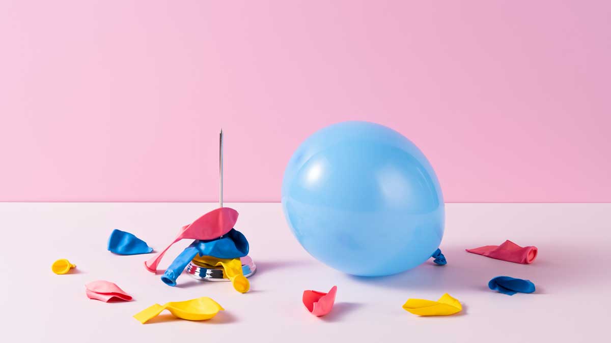 Ein blauer Luftballon vor rosa Hintergrund, daneben Reste bunter Luftballons, die von einer Nadel zerstochen wurden