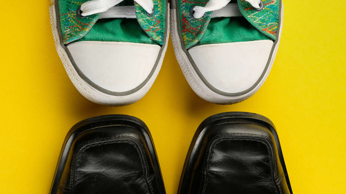 Grüne Converse Schuhe stehen Schuhspitze an Schuhspitze zu schwarzen Lederschuhen