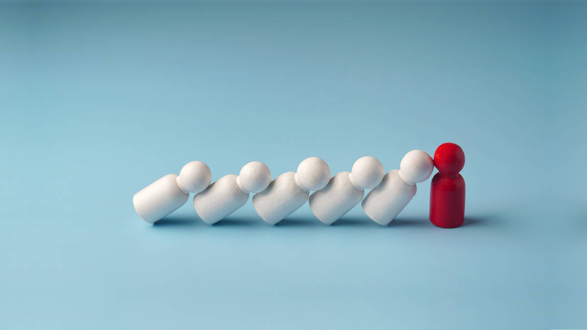 Weiße Brettspielfiguren kippen gegen eine rote und symbolisieren das Helfersyndrom von Chefs