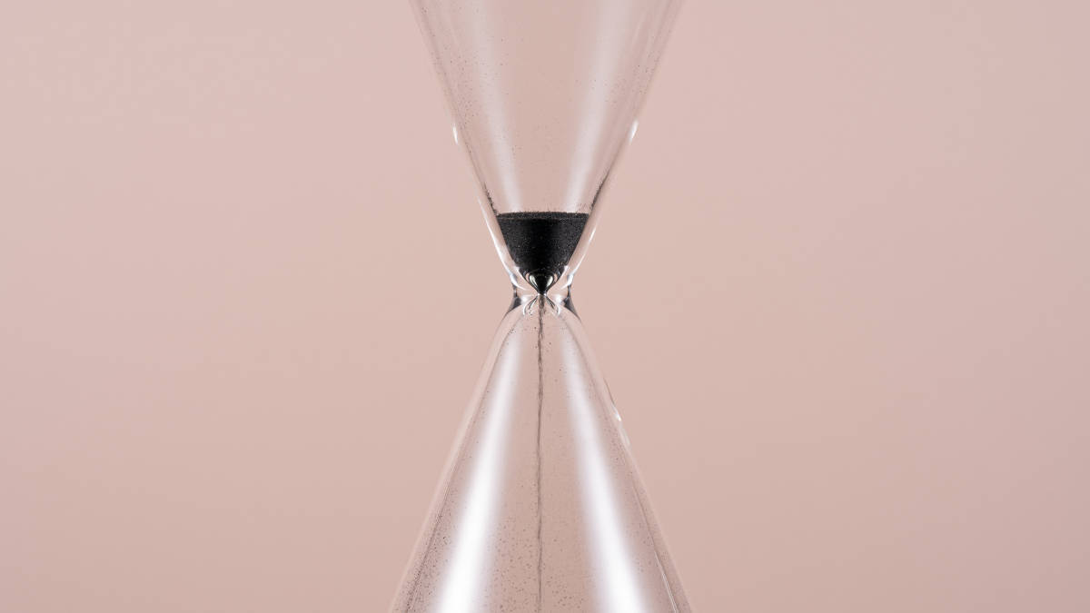 Mitte einer Sanduhr mit fast durchgelaufenem Sand auf rosa Hintergrund.