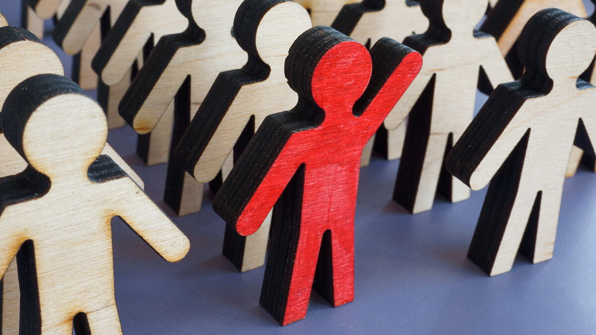 Holzmännchen stehen nebeneinander. In der Mitte steht ein rotes, das den Arm hebt.