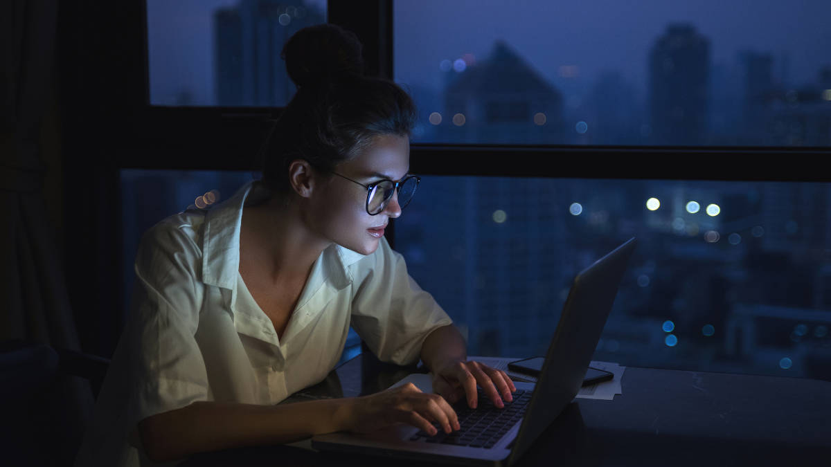 Frau arbeitet im Dunkeln am Laptop. Seitenansicht.