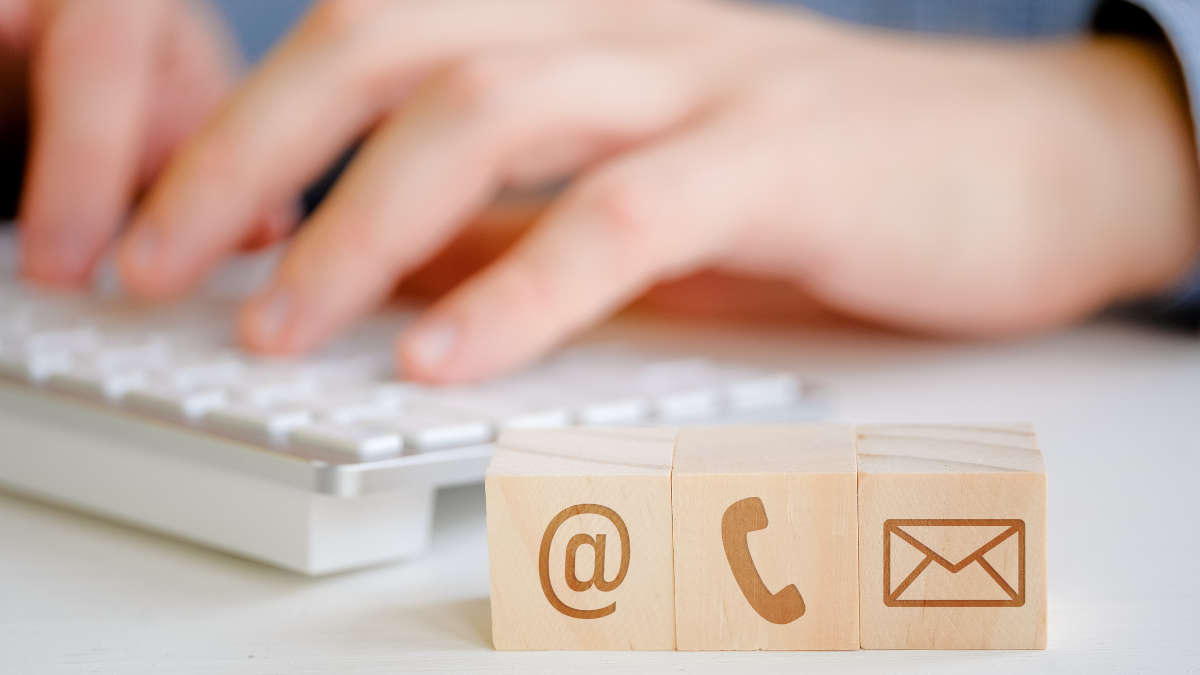 Im Hintergrund schreibt ein Mann auf einer Tastatur. Im Vordergrund sind 3 Holzwürfel mit Akquise Symbolen, sprich Mail, Telefon und Brief darauf.