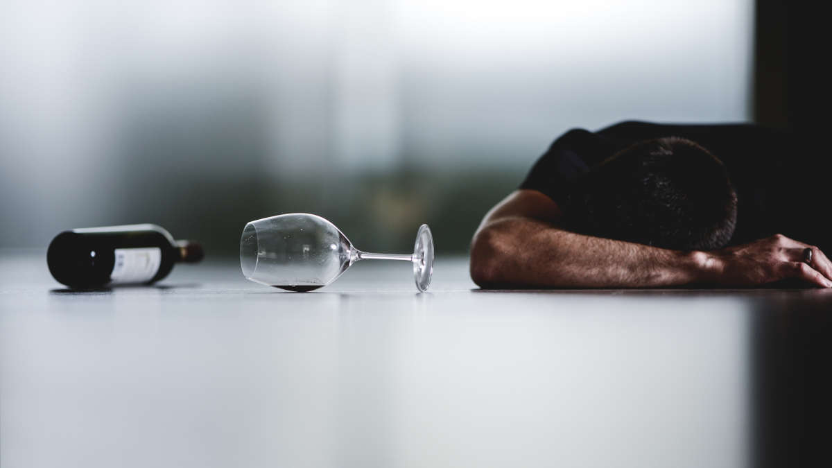 Bild eines schlafenden Mannes neben einer leeren Weinflasche und einem fast leeren Weinglas - als Illustration für jemanden, dem wegen Alkohol am Arbeitsplatz die Kündigung drohen könnte.