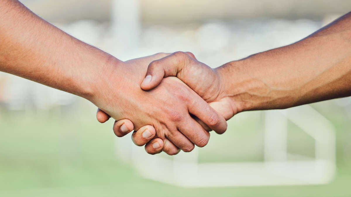 Handschlag mit einem Fußballplatz im Hintergrund.