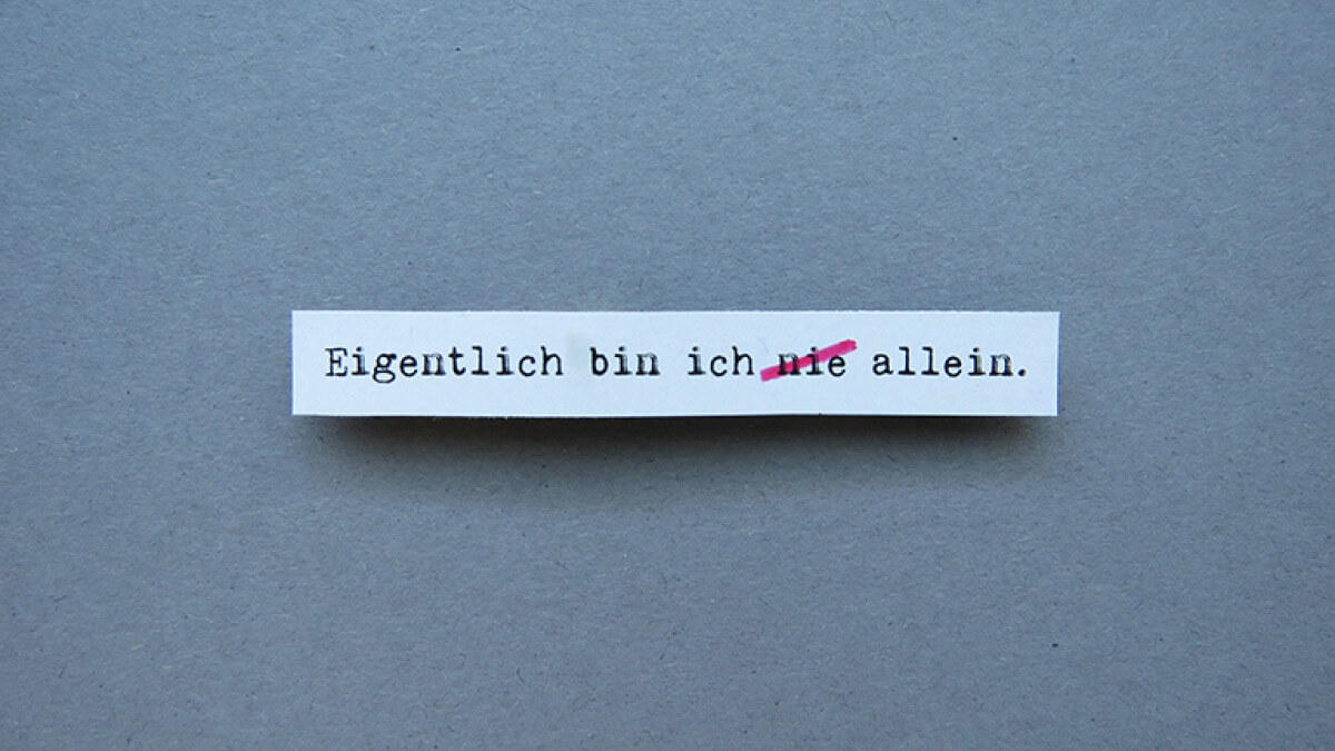 Schriftzug "Eigentlich bin ich nie allein" mit durchgestrichenem nie auf blau-grauem Hintergrund.