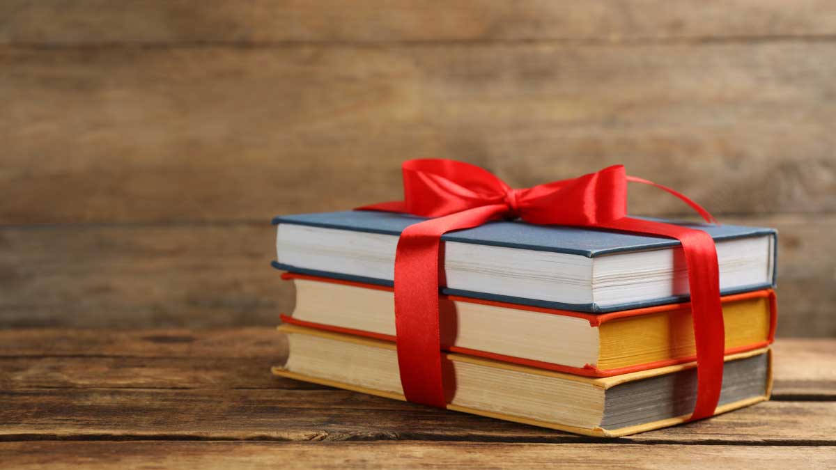 Drei Bücher, mit einer Schleife zusammengebunden, auf einem Holztisch.