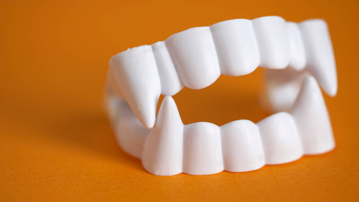 Vampirzähne aus Plastik vor einfarbigem Hintergrund.