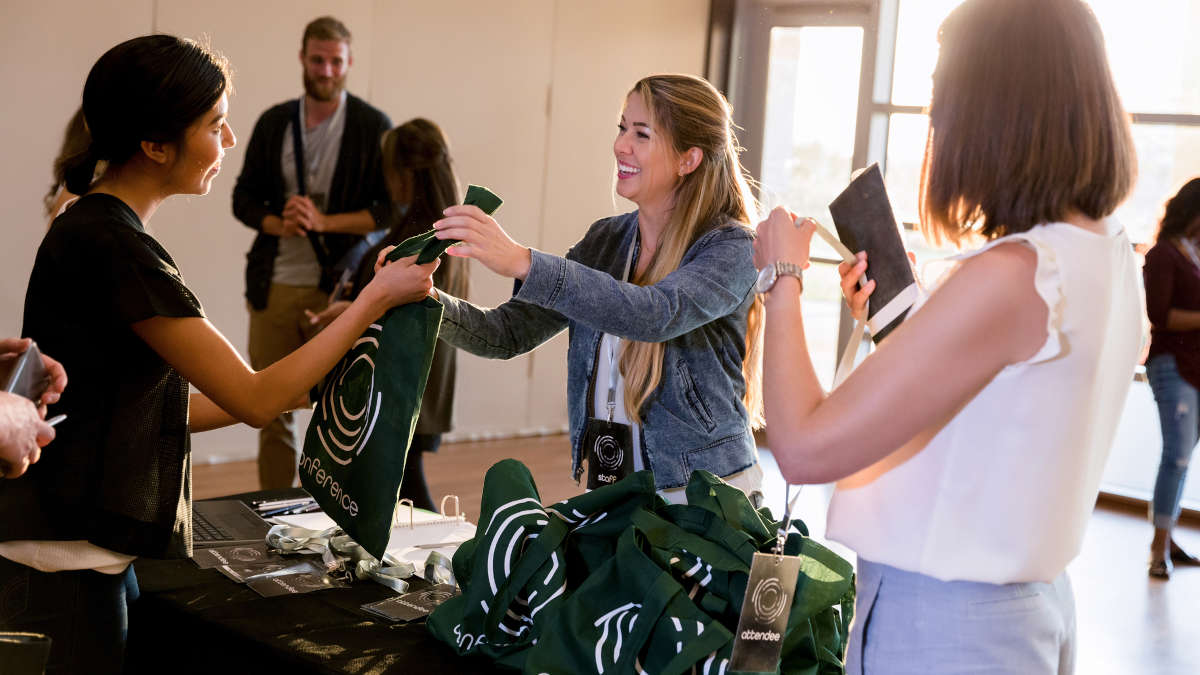 Eine Frau die einer anderen Frau einen Beutel mit Werbegeschenken übergibt