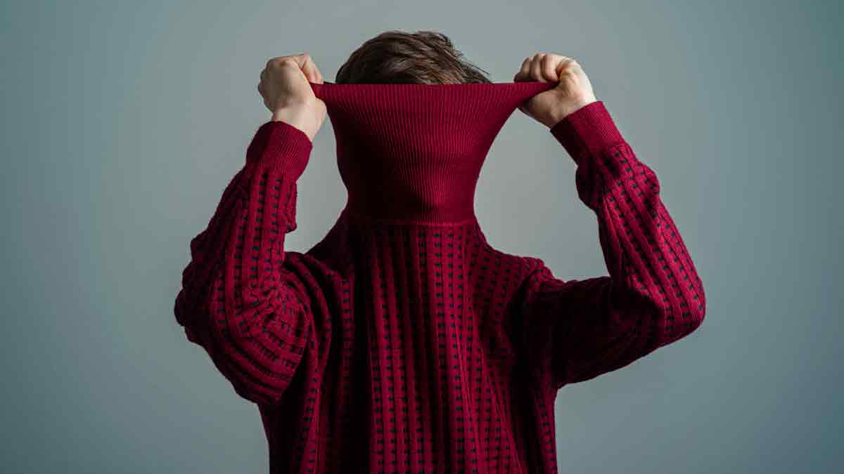 Eine Person hat sich den Rollkragen ihres roten Pullovers über das Gesicht gezogen.