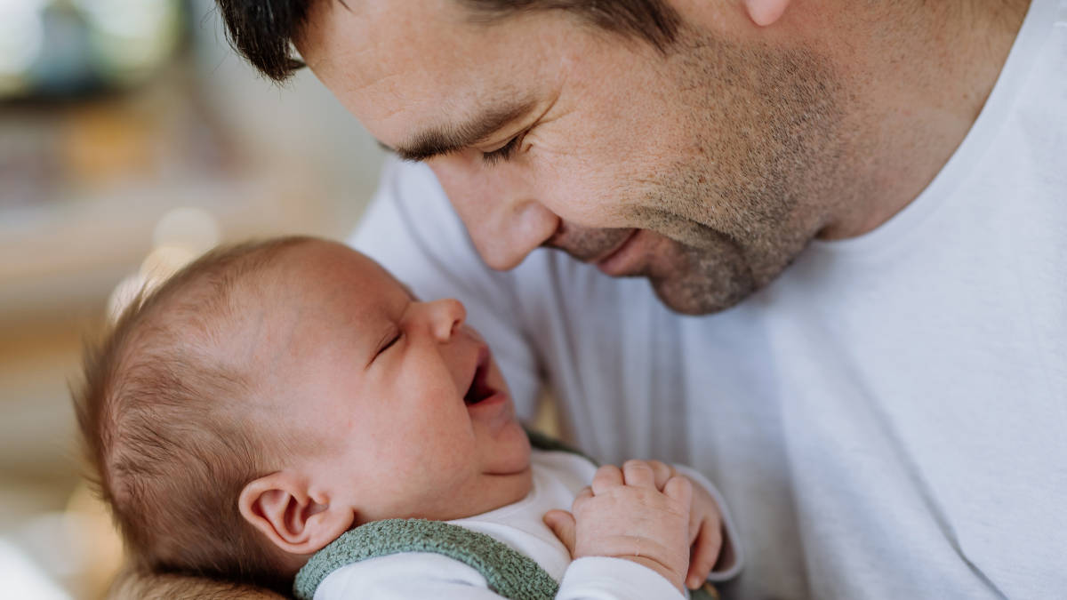 Ein Vater mit einem Baby im Arm in Nahaufnahme: Käme der Vaterschaftsurlaub 2025, hätten zweite Elternteile mehr Zeit für solche Kuscheleinheiten.