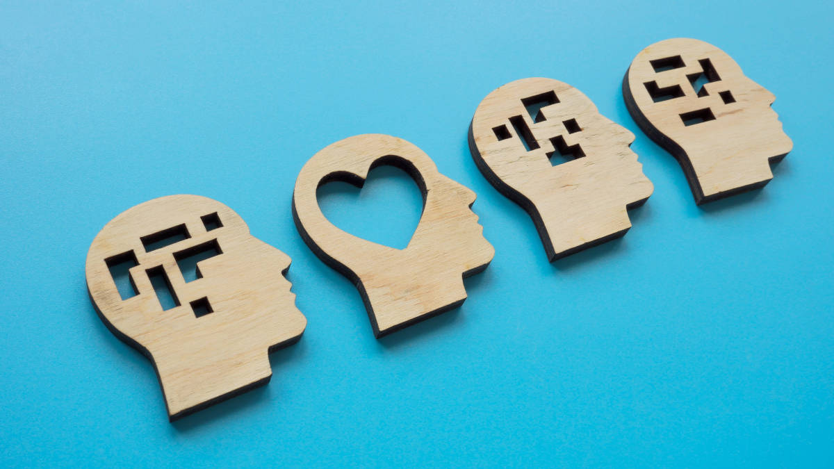 Bild von 4 Köpfen aus Holz im seitlichen Profil. Drei davon mit abstrakten Formen und eines mit einem Herzen am Ort des Gehirns.