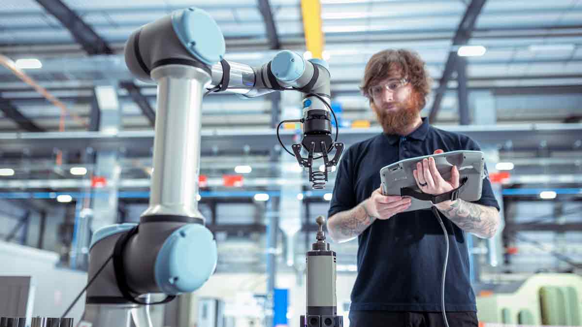 Ein Mann steuert mit einem Tablet in der Hand einen Roboterarm.