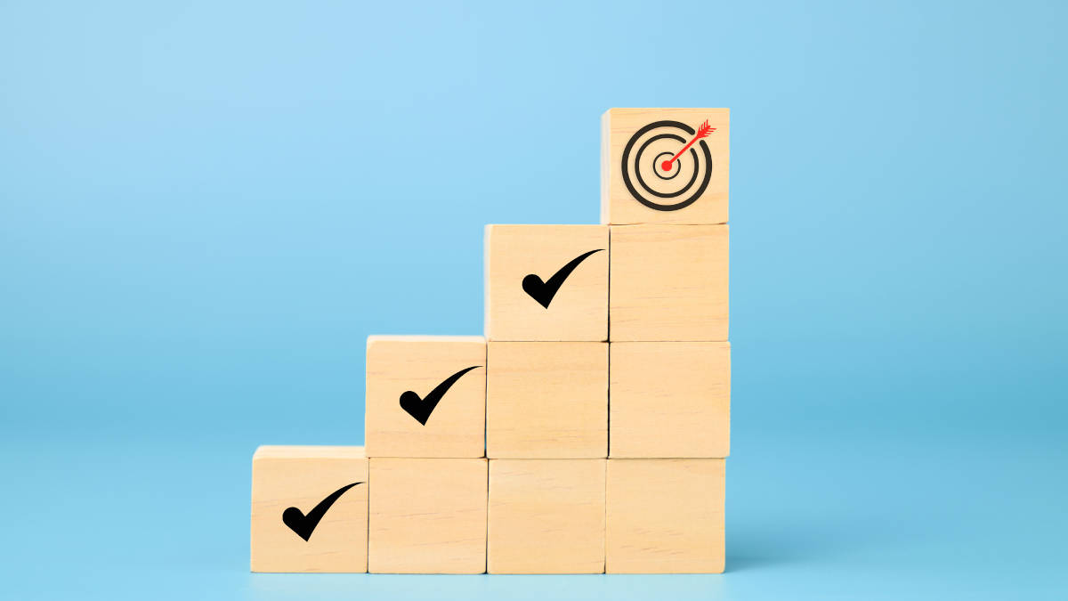 Eine Treppe aus Holzwürfeln mit Häkchen-Symbolen auf den Stufen und einer Zielscheibe ganz oben