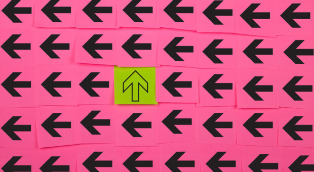 Viele schwarze Pfeile auf pinkem Hintergrund, die nach links zeigen mit einem gelben Pfeil auf gelbem Hintergrund in der Mitte, der nach oben zeigt.