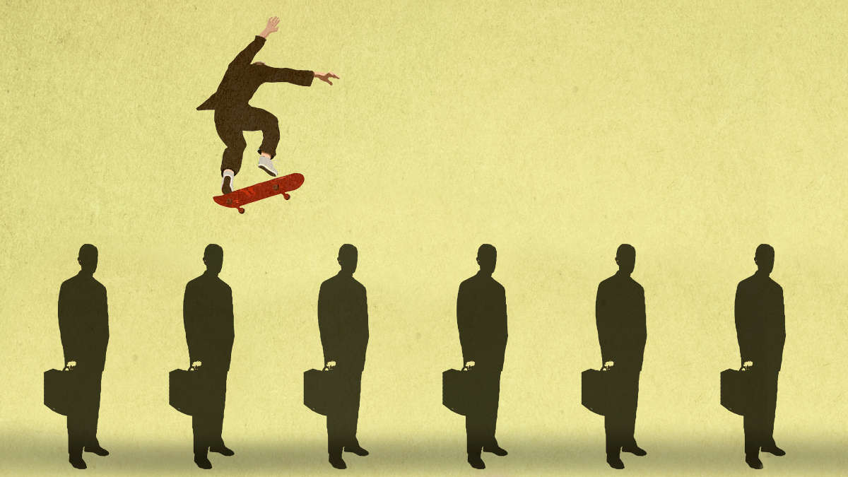 Eine Person mit Anzug springt mit einem Skateboard über sechs stehende Anzug tragende Personen