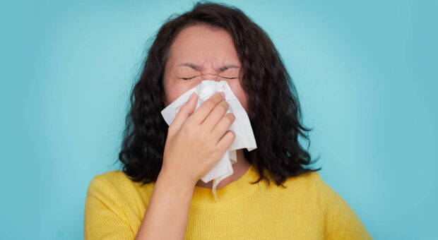 Frau die ins Taschentuch niest vor blauem Hintergrund.