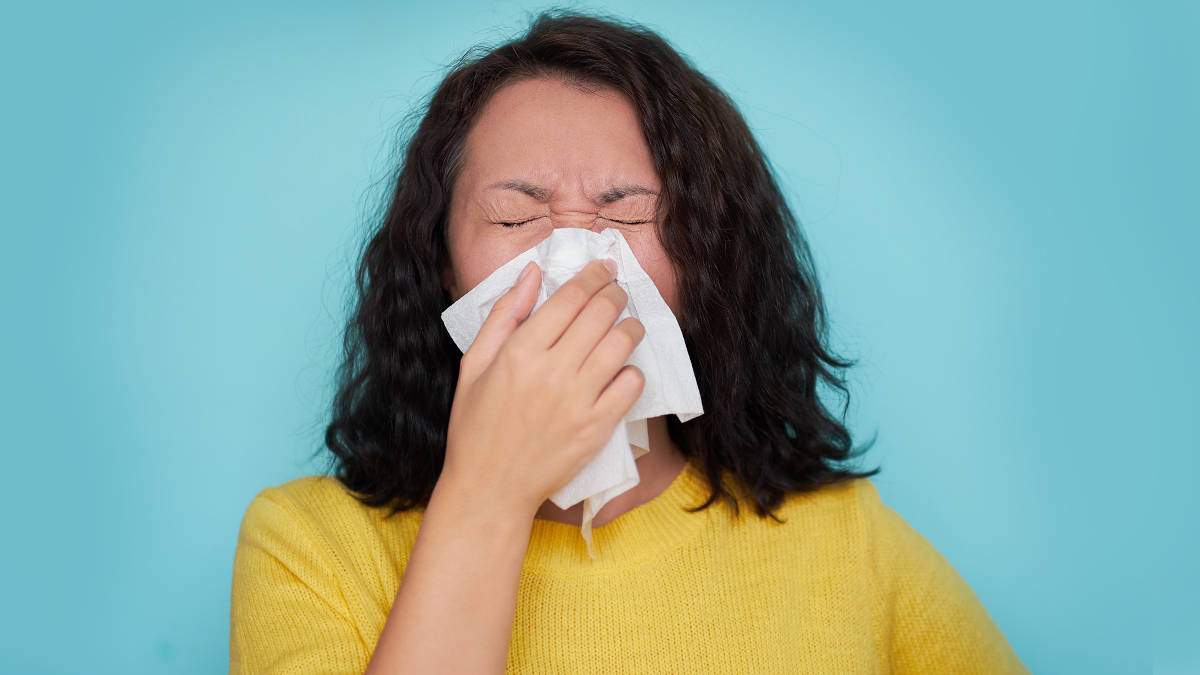 Frau die ins Taschentuch niest vor blauem Hintergrund.