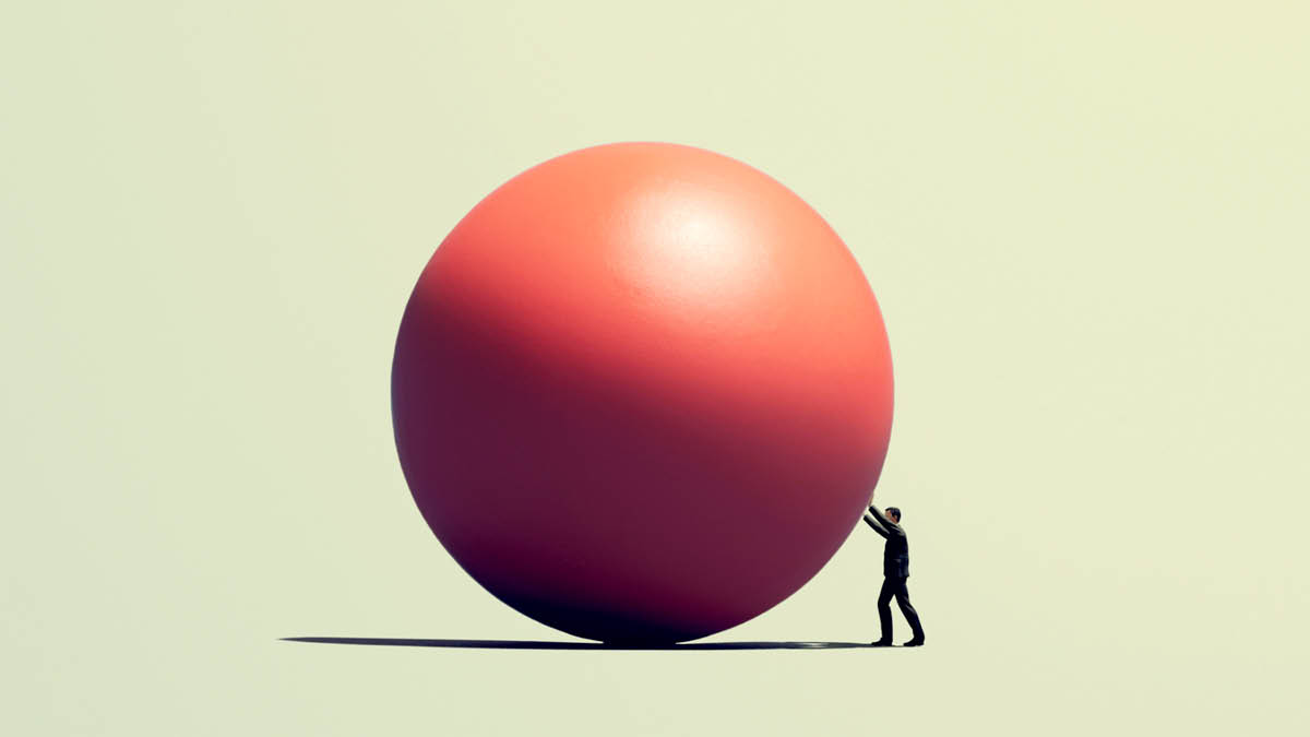 Eine Person versucht eine riesige rote Kugel zu rollen