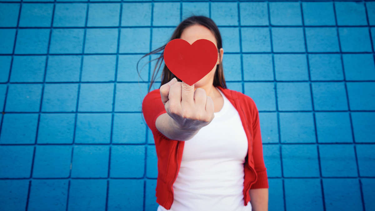 Eine Person streckt dem Betrachter ihren Mittelfinger entgegen, an dem aber ein rotes Herz befestigt ist