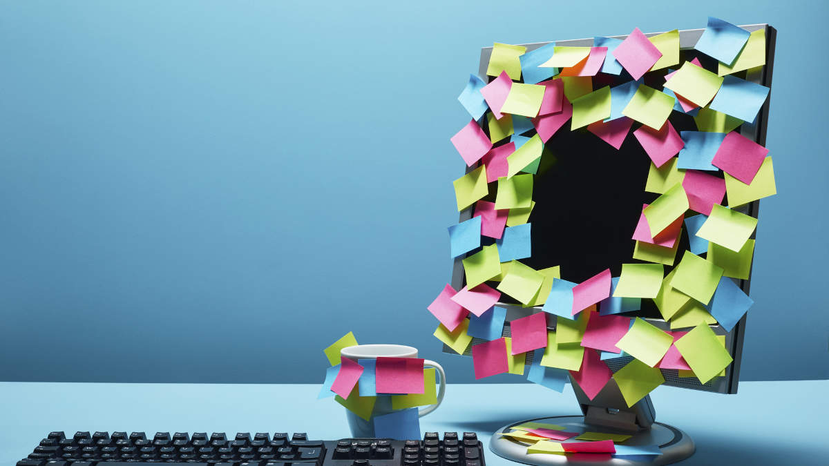 Schreibtisch im Büro. Der Bildschirm und die Tasse sind vollgeklebt mit bunten Post-Its.