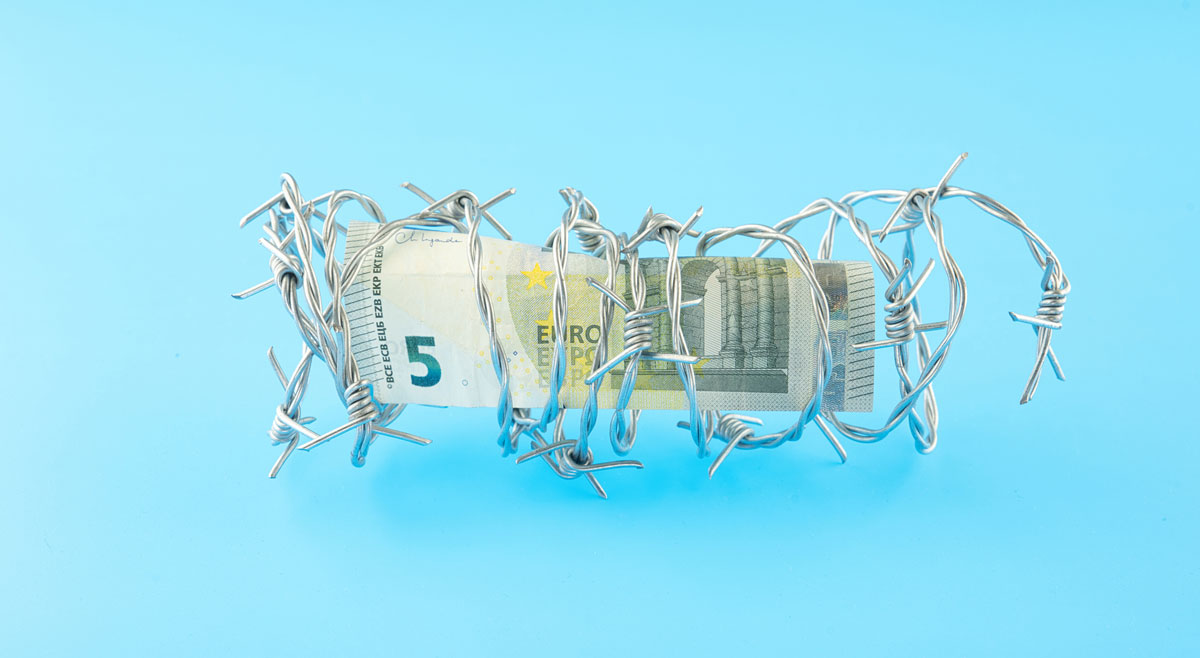 Geldschein, der von Stacheldraht eingehüllt wird, vor türkisfarbenem Hintergrund