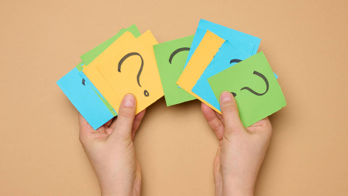 Zwei Hände die Post-Its mit Fragezeichen vor einem orangenen Hintergrund halten.