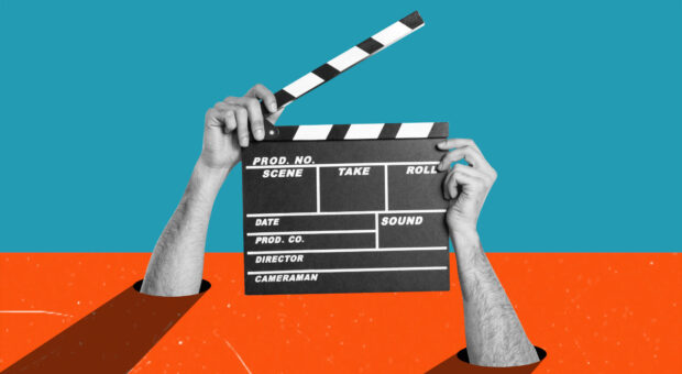 Hände, die aus einem Schreibtisch kommen und eine offene Filmklappe in der Hand halten