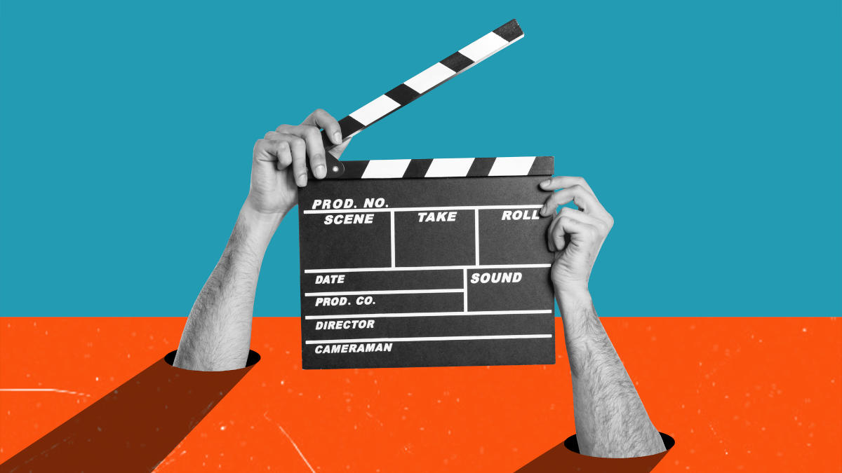 Hände, die aus einem Schreibtisch kommen und eine offene Filmklappe in der Hand halten