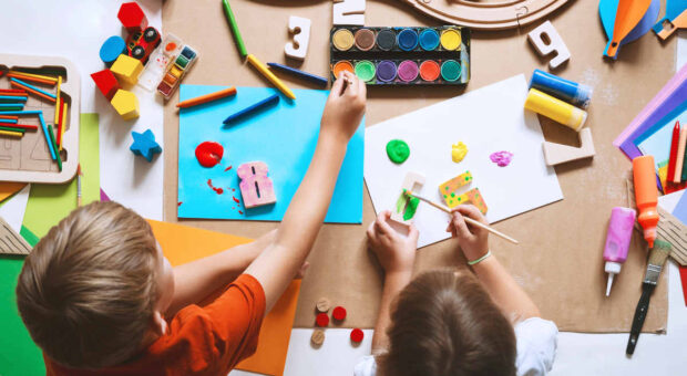 Vogelperspektive: Zwei Kinder malen und basteln an einem Tisch.