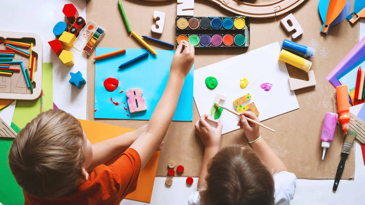 Vogelperspektive: Zwei Kinder malen und basteln an einem Tisch.