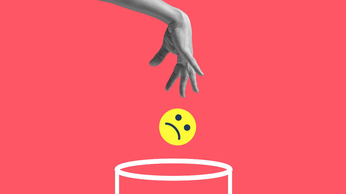 Eine Hand wirft einen schlecht gelaunten Smiley in einen Mülleimer.