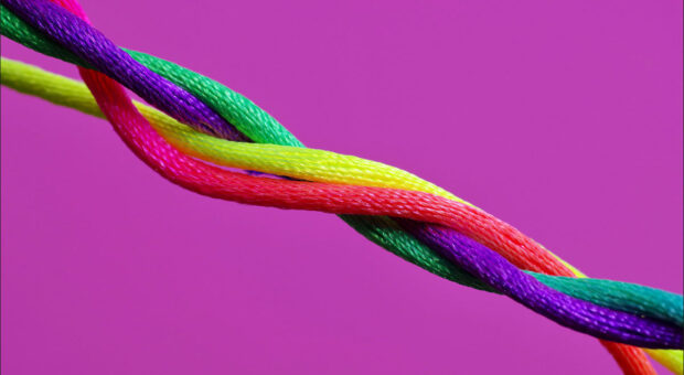 Ein Draht aus verschiedenen, bunten Strängen vor knalligem lila Hintergrund.