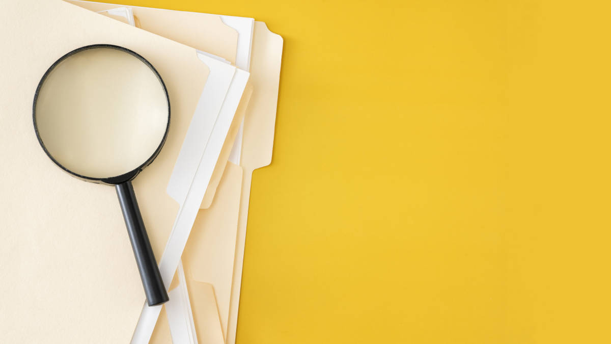 Eine Lupe liegt auf einem Stapel Unterlagen vor knallig gelbem Hintergrund