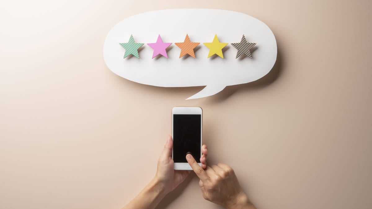 Eine Hand tippt auf ein Smartphone. Darüber ist eine Sprechblase mit fünf verschiedenfarbigen Sternen zu sehen.