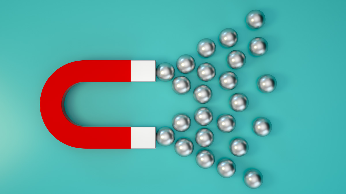 Ein roter Hufeisenmagnet, der Metallkugeln anzieht. Türkiser Hintergrund.