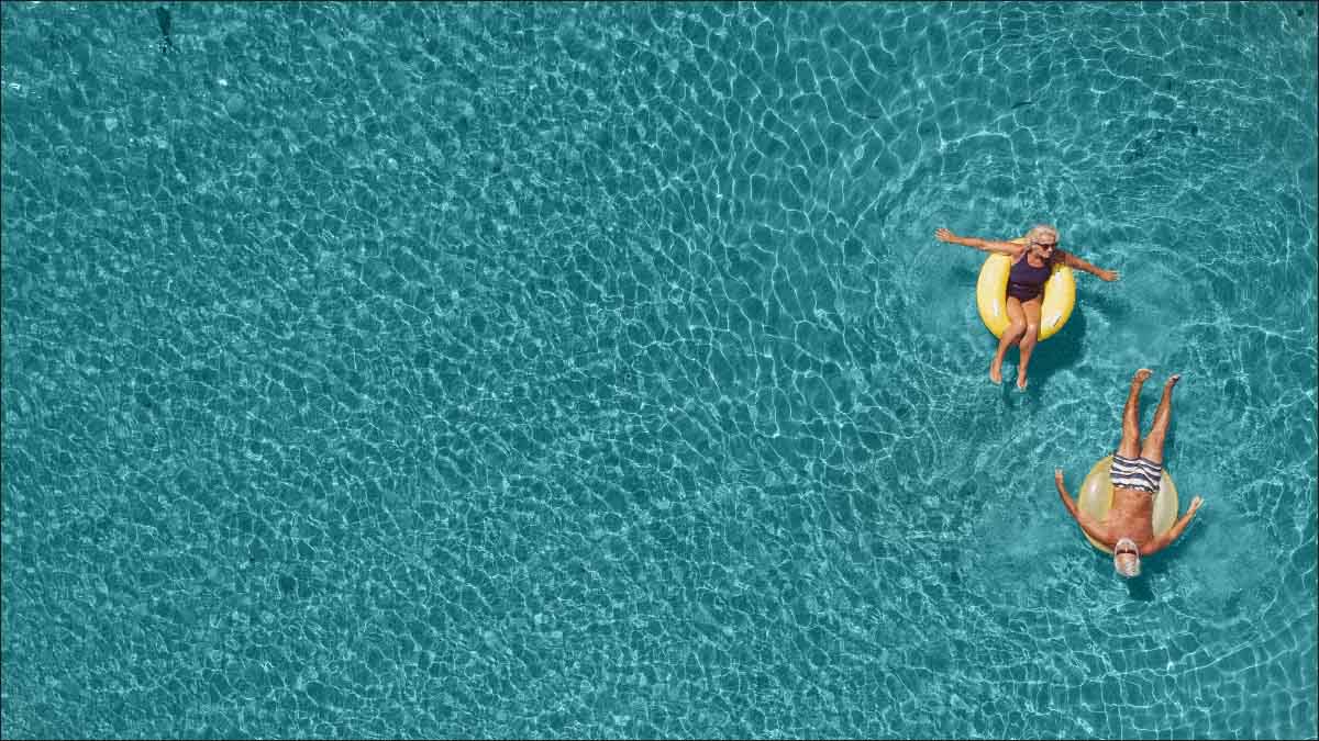 Vogelperspektive: Zwei ältere Menschen liegen in großen Schwimmreifen in klarem Wasser