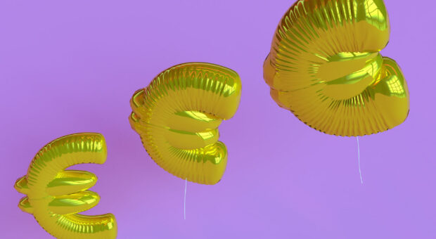 Drei goldene Luftballons in Form des Euro-Zeichens vor lila Hintergrund.