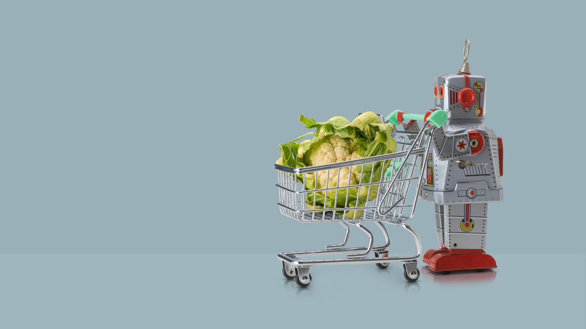 Ein kleiner Roboter schiebt einen Einkaufswagen mit einem überdimensionalen Blumenkohl
