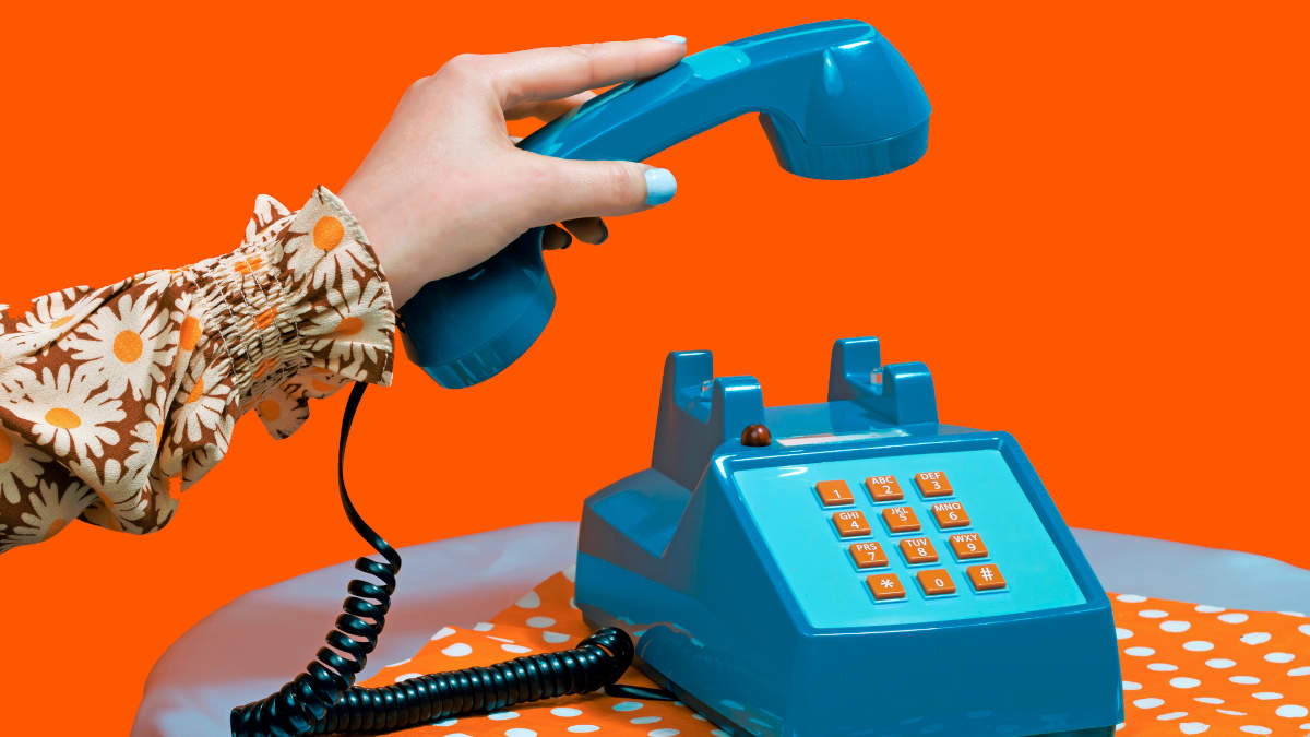 Eine Hand hebt den Hörer eines blauen altmodischen Telefons ab. Orangener Hintergrund.