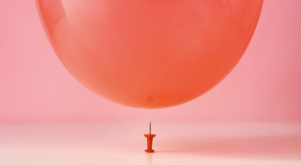 Luftballon, der über einer mit der Spitze nach oben stehenden Stecknadel schwebt.