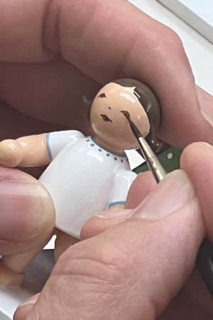 Detailaufnahme eines Holzengels, dem mit einem feinen Pinsel per Hand ein Auge aufgemalt wird.