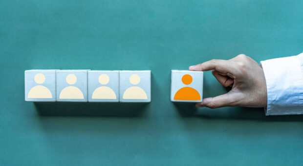 5 Würfel mit den Umrissen von Personen darauf. Eine Hand hält einen der Würfel.