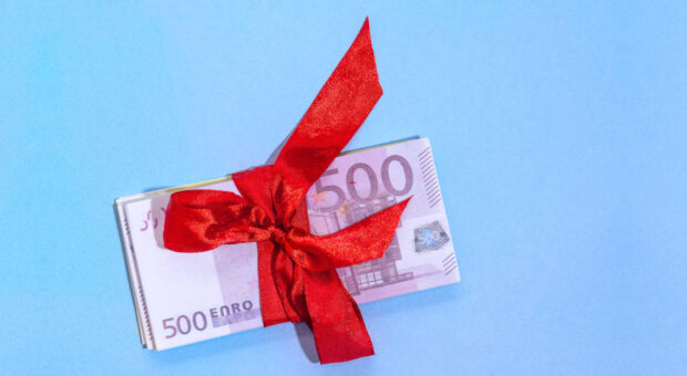 Fünfhundert-Euro-Scheine mit roter Schleife auf hellblauem Hintergrund.