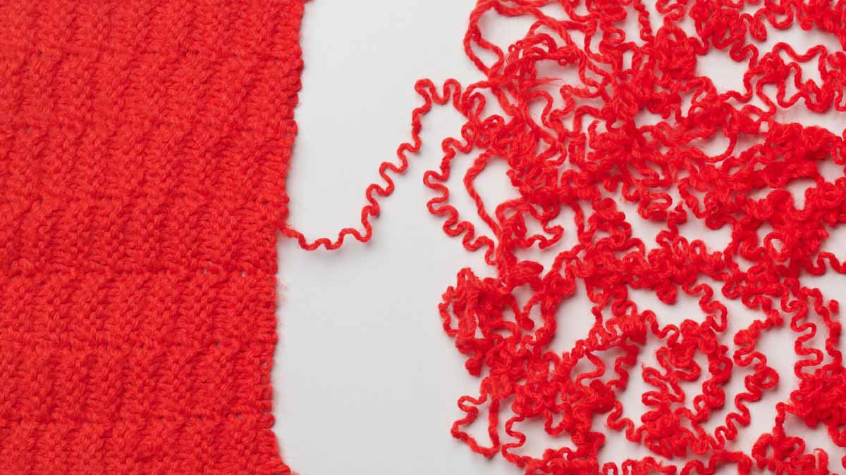 Rotes Gewebe, bei dem sich der Faden löst, auf weißem Hintergrund.